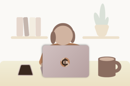 A person wearing headphones and using a laptop on a table with a smartphone and a cup of coffee