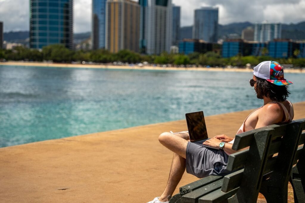 Man enjoying leisure time by the city waterfront with a laptop.