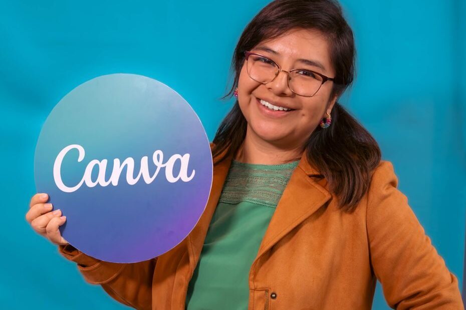A smiling woman in a casual outfit holds a Canva sign, posing confidently against a vibrant blue backdrop.